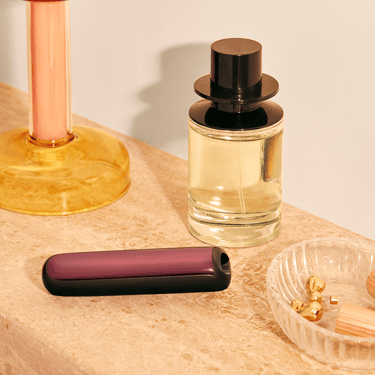 Ploom AURA priekšējais panelis Dark Orchid piestiprināts pie ierīces uz kosmētikas galdiņa

