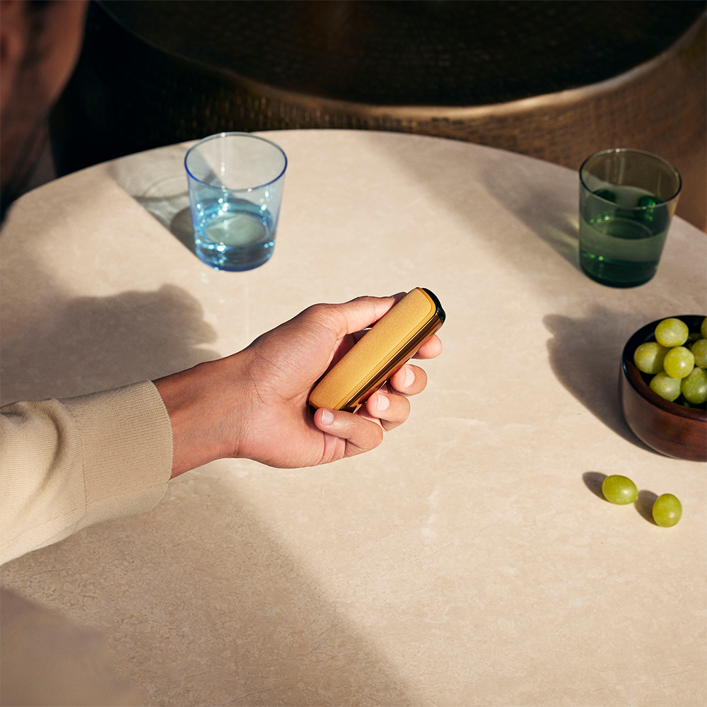 Roka rāda Ploom AURA ierīci ar pievienotu Mango Sorbet aizmugurējo vāciņu
